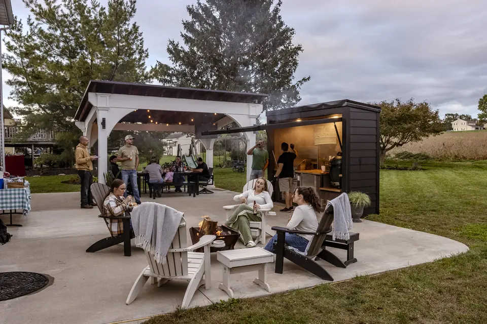 Friends and family gathered around the firepit with the Flamehouse open at dusk