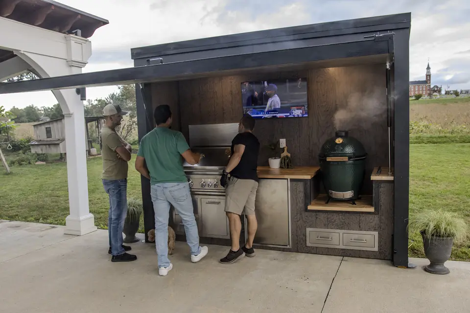 Friends gathered around an open Flamehouse, checking out the grill with the game on