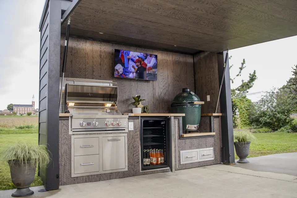 An open Flamehouse with grill, ceramic egg, TV, and a fridge stocked with drinks